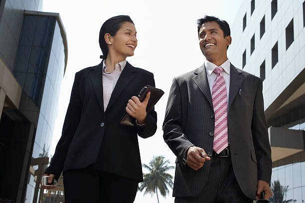 Man and a woman with business suits smiling and walking Low angle view of businesswoman and businessman walking outdoors indian women walking stock pictures, royalty-free photos & images