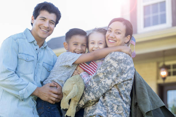 Man and his children are reunited with military mom Smiling family look at the camera while embracing. The mom has returned from military assignment. The little girl is holding a small US flag. arrival photos stock pictures, royalty-free photos & images