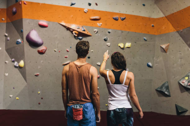 Man and woman at an indoor rock climbing gym Rear view of female instructor giving instructions to a man on wall climbing. Man learning the art of rock climbing at an indoor climbing centre. bouldering stock pictures, royalty-free photos & images