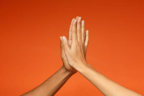 Man and woman greeting each other with high five African-american man and woman greeting each other with high five, clapping hands on orange background high five stock pictures, royalty-free photos & images