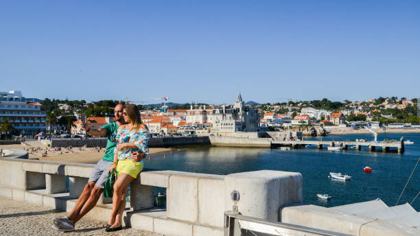 Man and woman pose for a selfie overlooking the gorgeous seaside cityscape of Cascais in summer day Cascais, Portugal - Sept 20, 2018: Man and woman pose for a selfie overlooking the gorgeous seaside cityscape of Cascais in summer day fomo photos stock pictures, royalty-free photos & images
