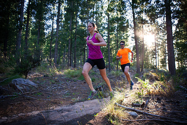 Man and woman running in the forest early morning Man and woman running in the forest early morning, the woman runs just infant the man on the rocky path. cross country running stock pictures, royalty-free photos & images