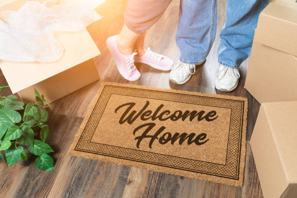 Man and Woman Unpacking Near Welcome Home Welcome Mat, Moving Boxes and Plant stock photo