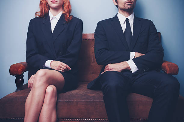 Man and woman waiting on a sofa Two sharply dressed business people are waiting on a sofa with a serious expression on their faces. Maybe they're waiting to enter a job interview, or maybe they're a couple waitng to see a divorce lawyer gender stereotypes stock pictures, royalty-free photos & images