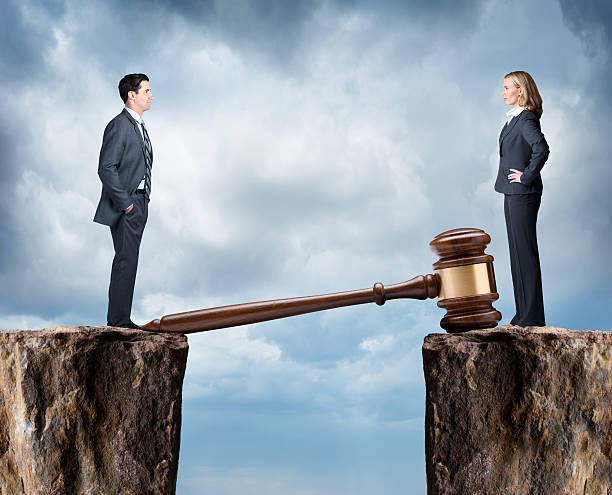 Man And Woman With Opposing Legal Points Of View A businessman and a businesswoman stand while facing each other as they stand on opposite cliffs which are bridged by a large gavel.  They are having a legal disagreement that could be related to business or personal issues that can only be remedied through the courts. divorce lawyer stock pictures, royalty-free photos & images