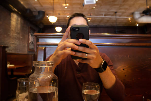 Man at a restaurant using smart phone Hands with smart phone blocking the face of the user in a restaurant with water and beer glasses on the table bad date stock pictures, royalty-free photos & images