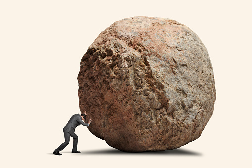 A man leans into his effort to push a giant round boulder.