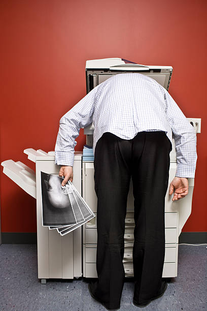 Man bending over the photocopier to Photocopy his face Business man bending over the office photocopier and makes copies of his face and make a few prints showing a humorous moment while working at the office xerox photocopy machine stock pictures, royalty-free photos & images