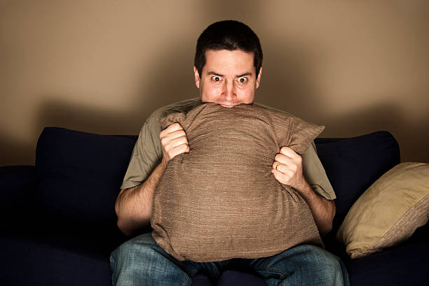 Man bites pillow in fear while watching TV stock photo