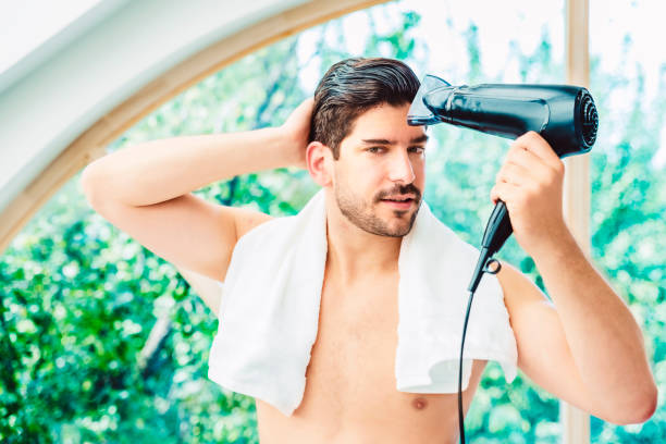男は自宅のバスルームで朝に髪を乾燥させる吹く ストックフォト