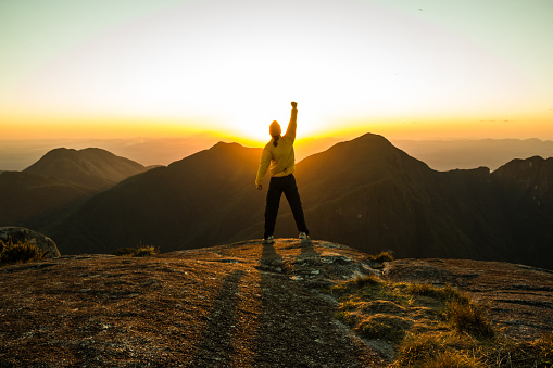 Man celebrating success on top of a mountain with one arm Raised and Hands Closed