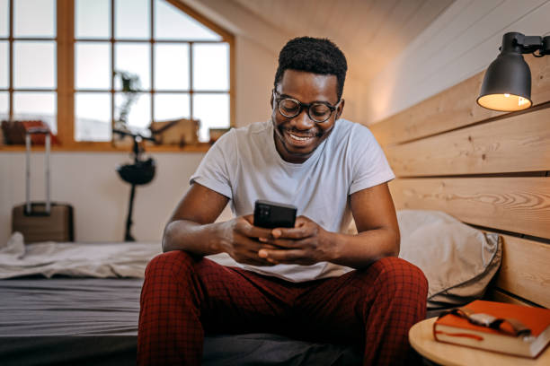 Man checking smartphone sitting on bed at night stock photo