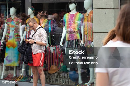 Man checks his mobile phone for a window with mannequins in rainbow clothes