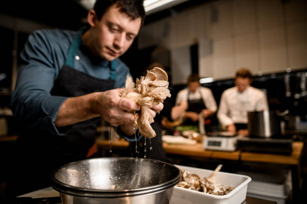 man chef holds oyster mushrooms over bowl on kitchen man chef holds handful of oyster mushrooms in his hands from which drops of water flow down into bowl on kitchen oyster mushroom stock pictures, royalty-free photos & images
