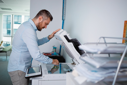 Man standing by the photocopier in the office and cleaning glass before making copies of documents