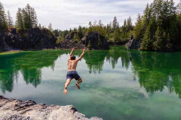 Man Cliff Jumping into a Lake Athletic and Adventurous Man is Cliff Jumping into a Green Colored Glacier Lake during a hot and sunny summer day. Taken in British Columbia, Canada. cliff jumping stock pictures, royalty-free photos & images