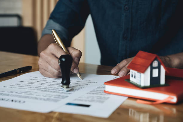 homme signant un document avec un stylo avec un livre et une petite maison dessus 