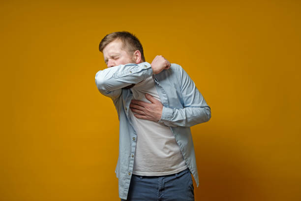 Man coughs in his elbow and holds hand on chest, experiencing pain. Concept of the spread of the virus. stock photo
