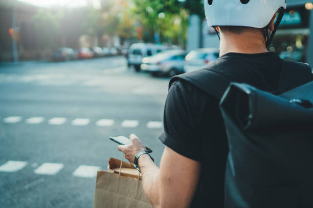 Man courier using a map app on mobile phone to find the delivery address in the city. Anonimous Courier delivery food service at home. stock photo