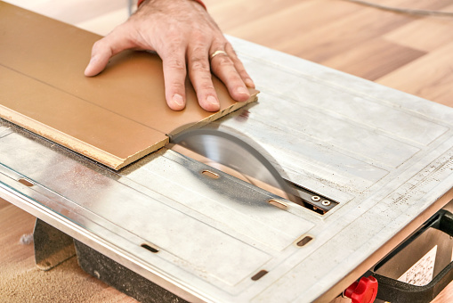 Man Cutting Laminate Floor Boards On Circular Saw Detail On Hands