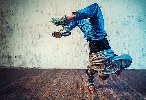 Young man break dancing on wall background. Vibrant colors effect.