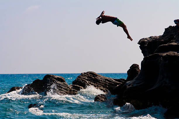 A man diving off a cliff and into the ocean A man that is jumping from the rocks into the sea cliff jumping stock pictures, royalty-free photos & images