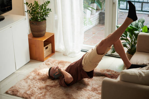 Man Doing Bridge Pose Young man talking on phone, leaning on couch when doing bridge pose at home pelvic floor stock pictures, royalty-free photos & images