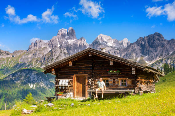 Man dressed in traditional Austrian or Bavarian clothes sitting on bench in front of alpine hut, enjoying beer in Alps Young man sitting on bench in front of alpine hut, Sulzenalm, Salzburger Land hut stock pictures, royalty-free photos & images