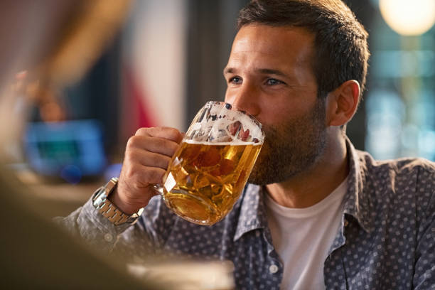 Man drinking a pint of draft beer Handsome young man drinking a pint of beer while looking away. Cheerful mid man in casual clothing feeling relaxed while enjoying draft beer in bar. Middle aged guy take a sip from his drink at pub during the night. artisanal food and drink photos stock pictures, royalty-free photos & images