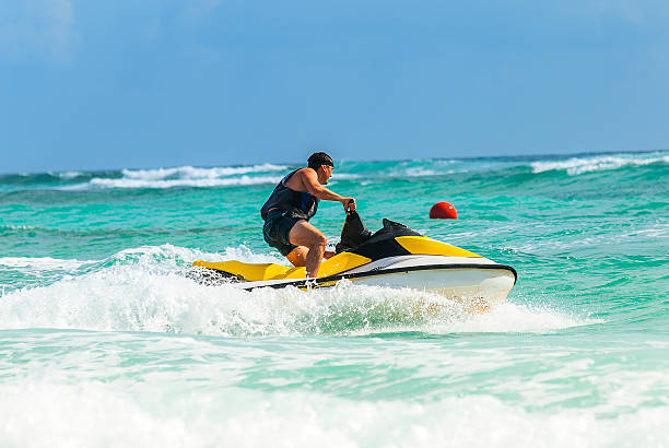 Man drives yellow jet ski on turquoise ocean on a blue day stock photo