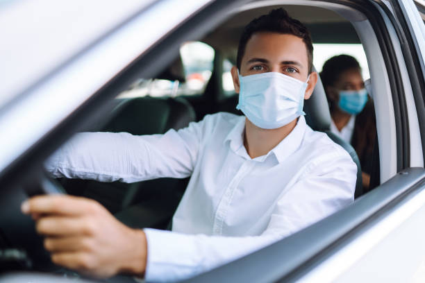 mann fährt ein auto in schützender steriler medizinischer maske während einer epidemie in quarantänestadt. covid- 19. - berufsfahrer stock-fotos und bilder