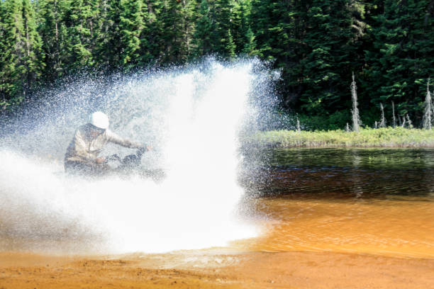 mann fährt motocross atv quad durch spritzenden fluss see wasser mit hoher geschwindigkeit. foy, foyross lake, sudbury, kanada. - motorrad fluss stock-fotos und bilder