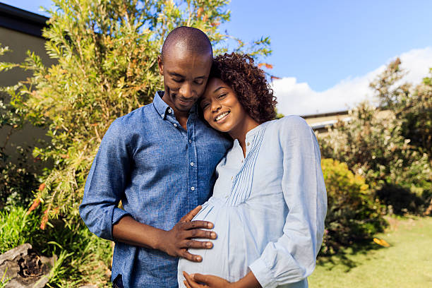 man embracing pregnant woman in yard - pregnant couple outside stockfoto's en -beelden