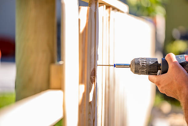 Man erecting a wooden fence outdoors Man erecting a wooden fence outdoors using a handheld electric drill to drill a hole to attach an upright plank, close up of his hand and the tool in a DIY concept. fence stock pictures, royalty-free photos & images