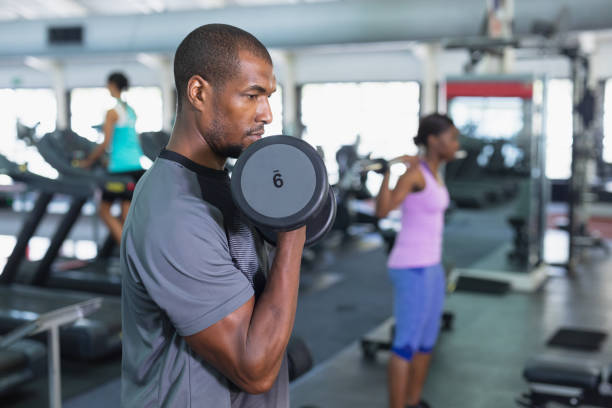 Man exercising with dumbbells in fitness center stock photo