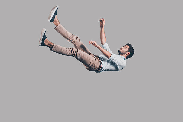 Man falling down. Mid-air shot of handsome young man falling against grey background levitation stock pictures, royalty-free photos & images