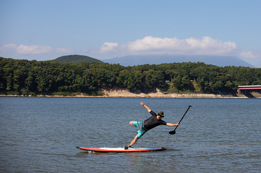 A man looses his balance and is falling off his stand up paddle board.