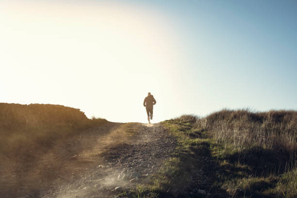 Man fell running in remote hillside location. Man fell running along a dry dusty dirt road in a remote rural location in late afternoon sunshine. escaping stock pictures, royalty-free photos & images