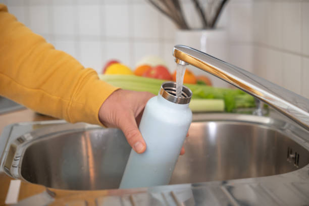 Man fills up reusable water bottle in the kitchen stock photo