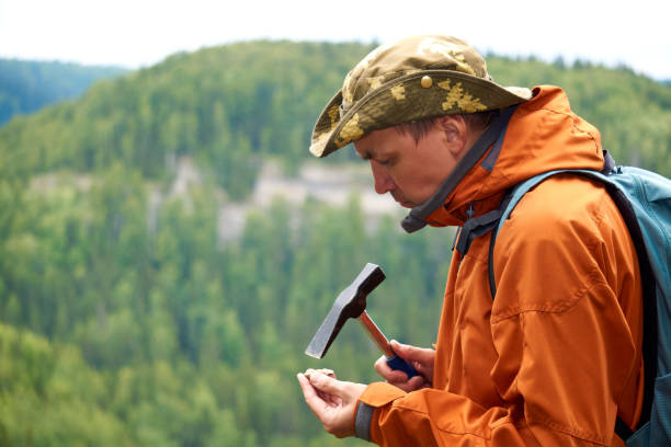 man geologist on an expedition examines a stone for hardness with a hammer man geologist on an expedition examines a stone for hardness with a geological hammer geologist stock pictures, royalty-free photos & images