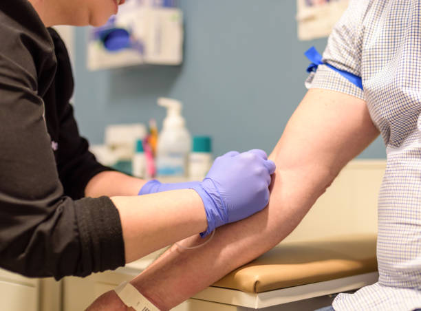 Man getting blood drawn at routine health screening Adult man getting blood drawn in exam room by healthcare worker blood testing stock pictures, royalty-free photos & images