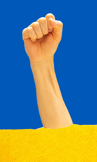 Man hand clenched in fist up in the air with blue and yellow colors in background. Raised up fist. Concept of unity, fight and cooperation.