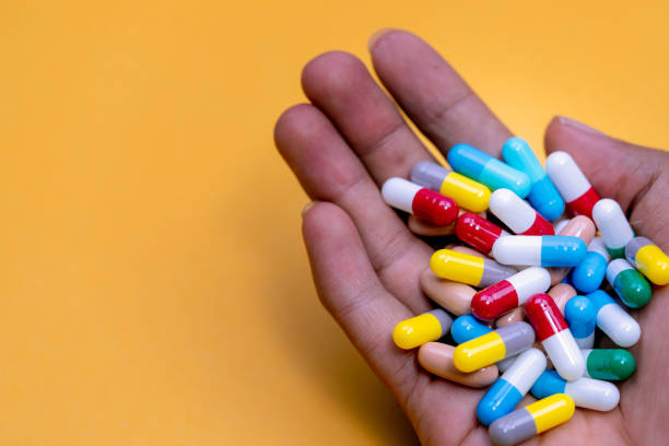 Man hand holding colorful capsule pills on yellow background. Prescription drugs. Drug overuse and polypharmacy concept. Drug allergy. Pharmaceutical industry. Pharmacy banner. Healthcare and medicine stock photo