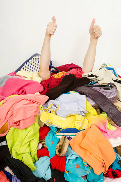 Man hands signing thumbs up under big pile of clothes. stock photo
