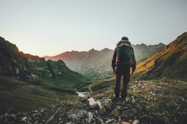 Man hiking at sunset mountains with heavy backpack Travel Lifestyle wanderlust adventure concept summer vacations outdoor alone into the wild stock photo