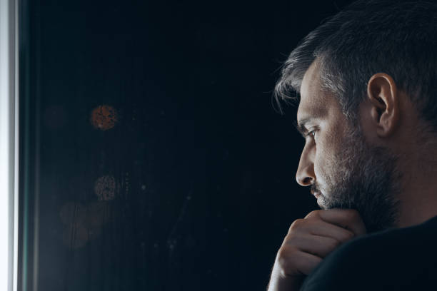 Man holding chin beside window Man with beard holding his chin beside window at night drug abuse stock pictures, royalty-free photos & images