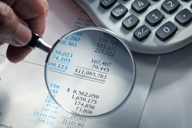 Man Holding Magnifying Glass Over Financial Report Close up of a man holding a magnifying glass over a financial report.  A calculator sits off to the side. bank statement stock pictures, royalty-free photos & images