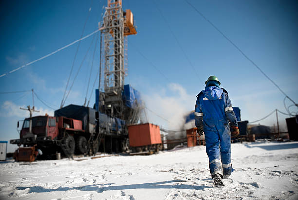 Man in a blue jumpsuit walking onto snowy construction site An engineer is walking towards the drilling rig. oil  stock pictures, royalty-free photos & images