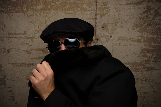 A man in a cap and dark glasses hides his face with his coat stock photo