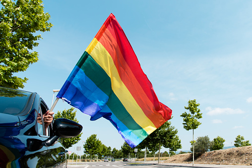 man in a car waving a rainbow flag